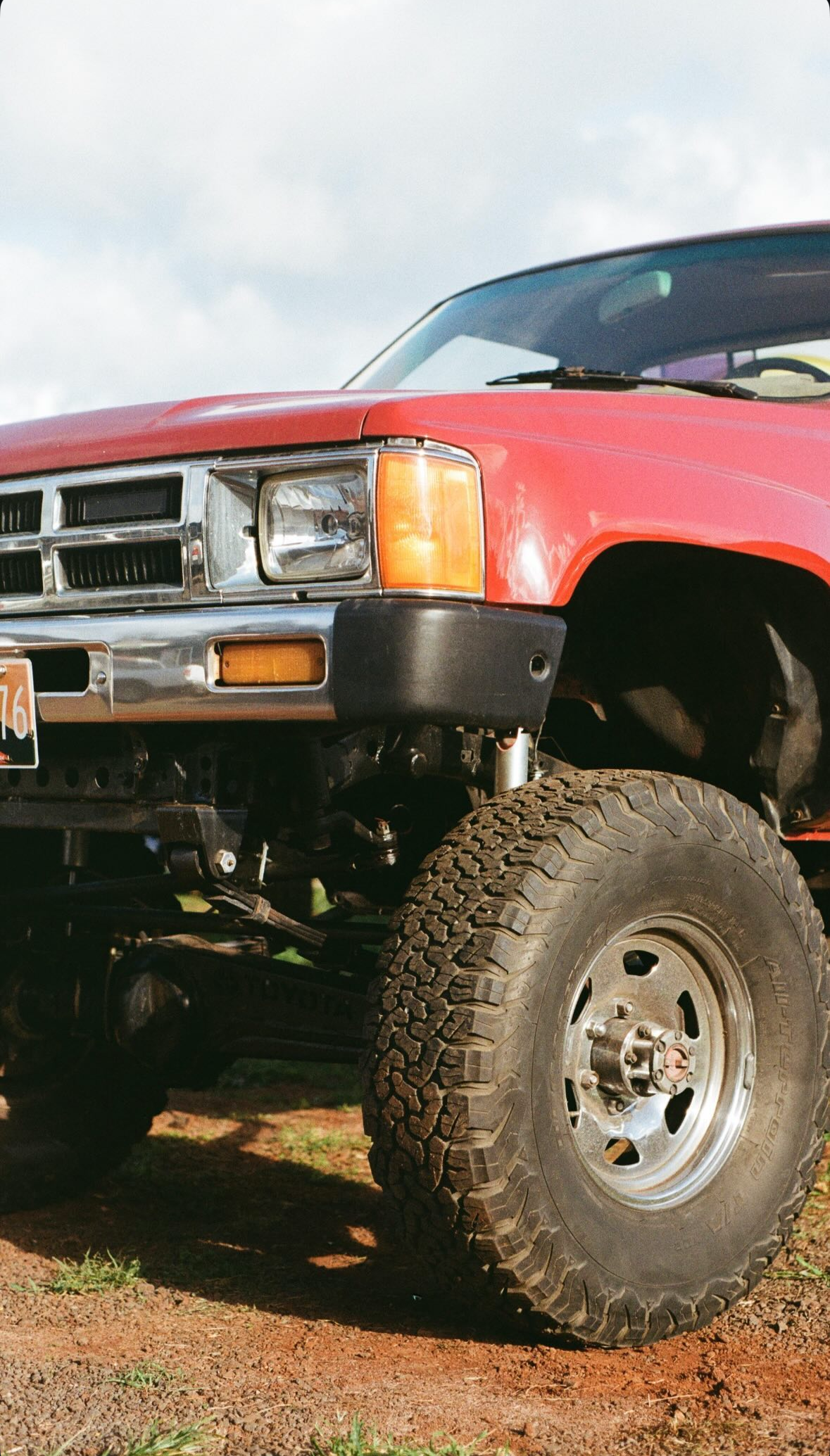 Red pickup truck with large off-road tires on a dirt road